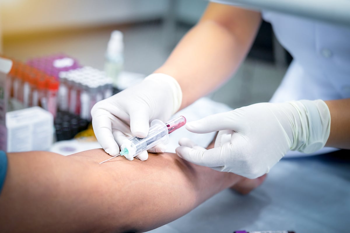 A phlebotomist's gloved hands drawing blood with a butterfly needle and vacuum collection tube