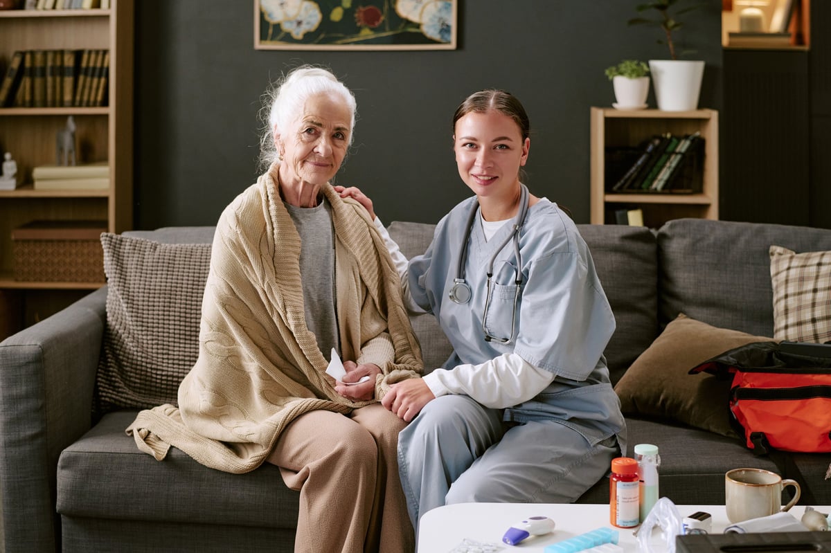 A nurse holding hands with a smiling senior patient at home, reflecting our in-home care